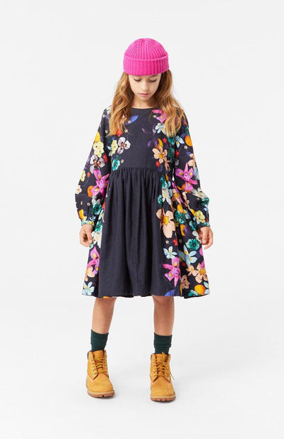 Girl wearing Black Como Vertical Garden Dress with long sleeves. The Sleeves are covered in flowers and the side of the dress has flowers. 