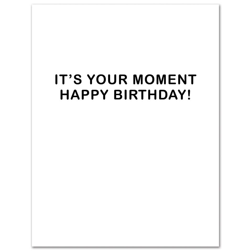 White card with black text 'IT'S YOUR MOMENT HAPPY BIRTHDAY!' on a white background