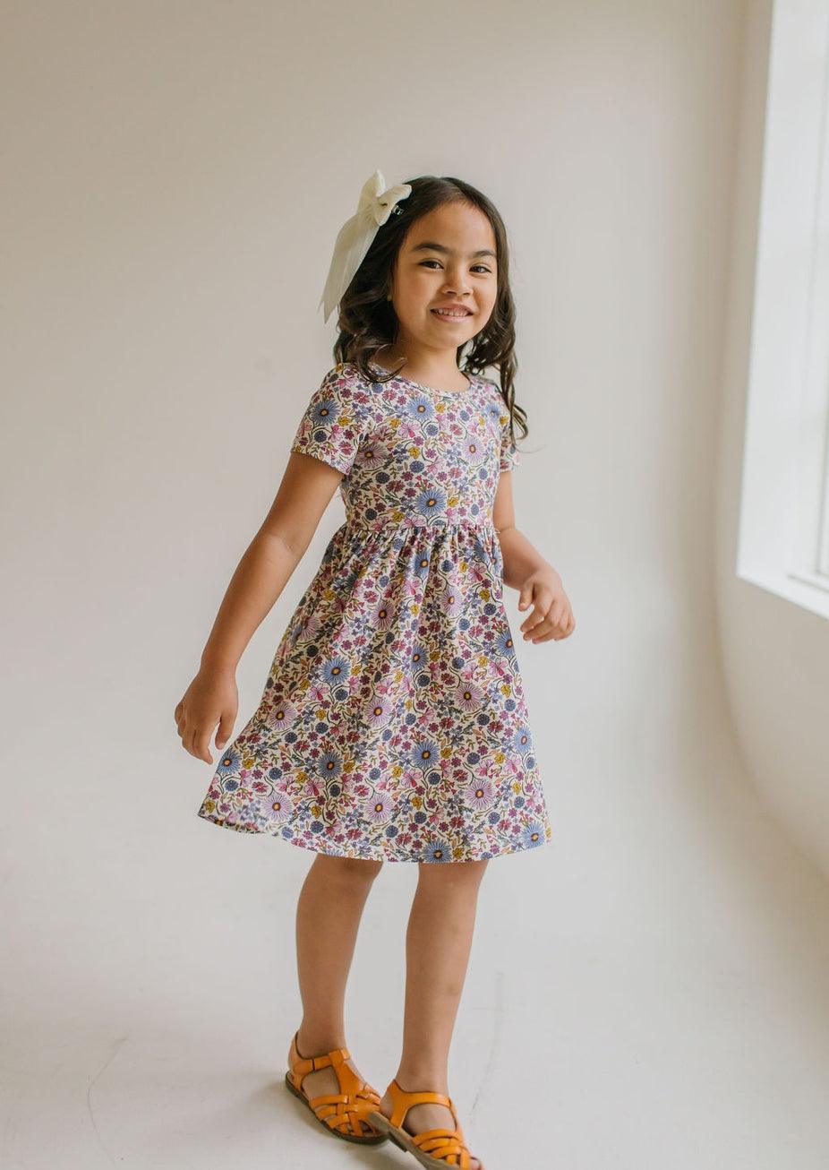 this picture shows the dress is short sleeve and floral with lavenders, purples and pops of gold and pink. 