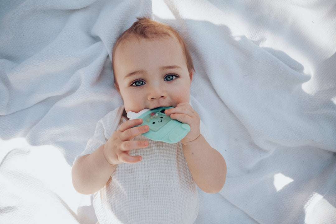 Baby holding a green teething ring on a white blanket