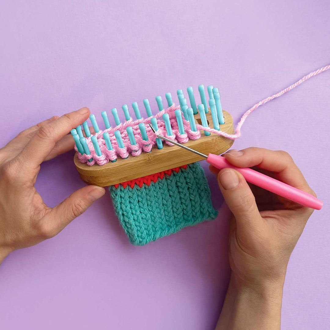 Person using a loom with pink and teal yarn on a purple background