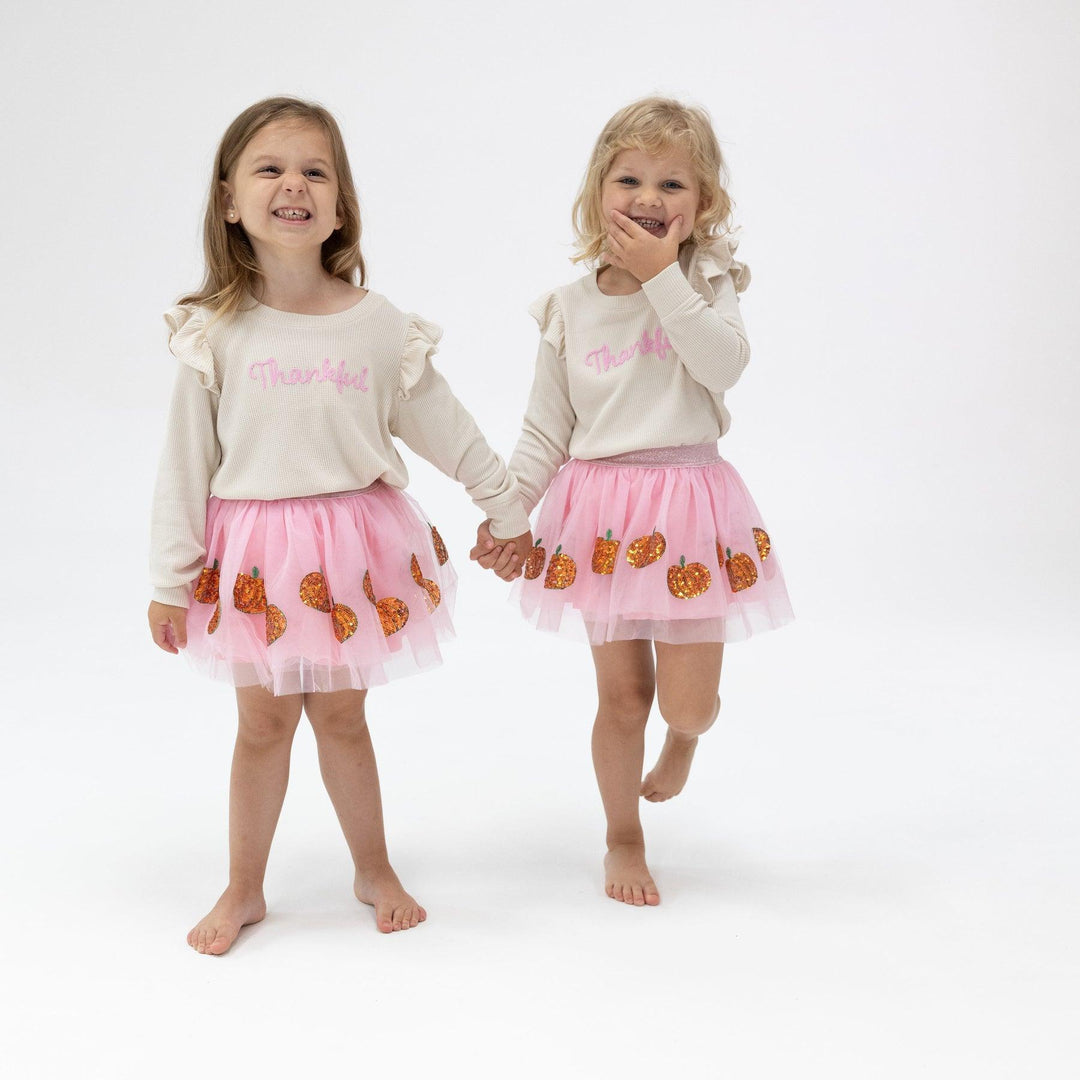 2 little girls modeling the thankful sweatshirt and pink tutu with orange pumpkins along the bottom of the skirt. the sweatshirt says thankful. 