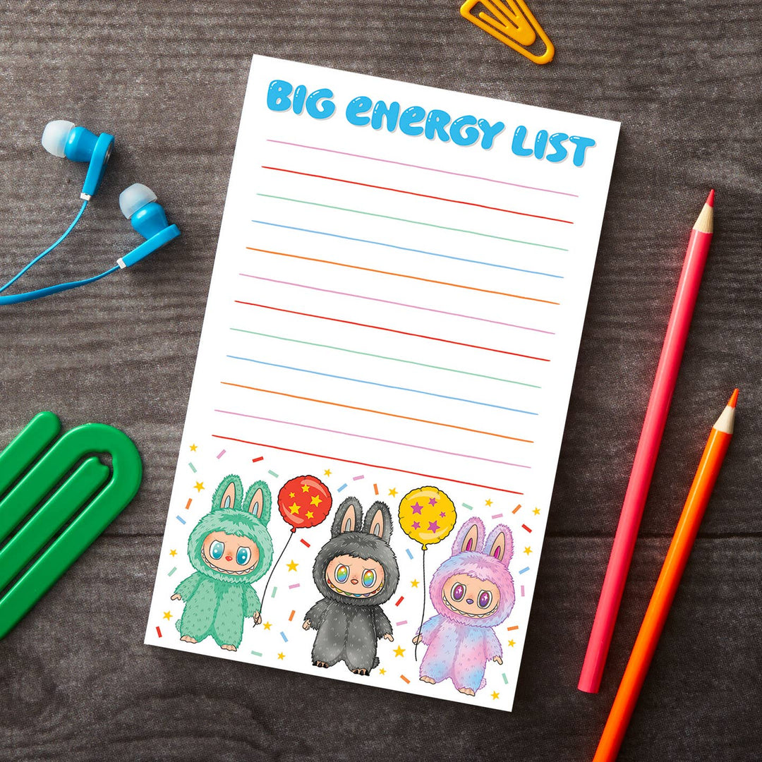 Notepad titled 'Big Energy List' with cartoon characters and balloons on a wooden surface with stationery items.