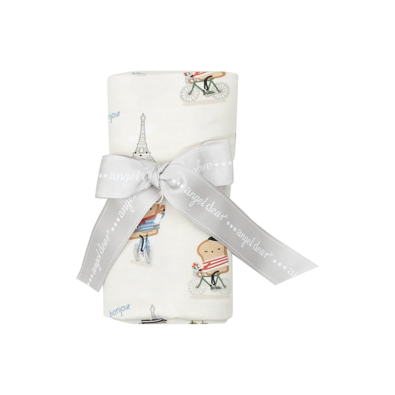 baby swaddle with pieces of toast dressed in French attire riding a bicycle in front of the Eiffel Tower. 