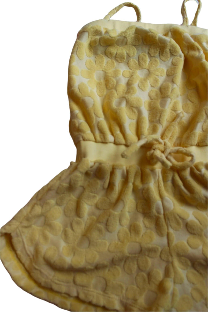 yellow terry romper with daisy printed embellishments all over the romper, spaghetti straps, elastic waist and tie at the waist. 