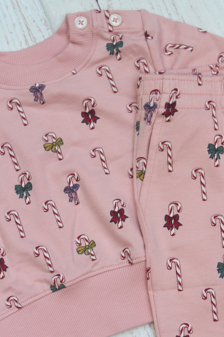 Pink children's outfit with candy cane and bow pattern on a light wooden surface