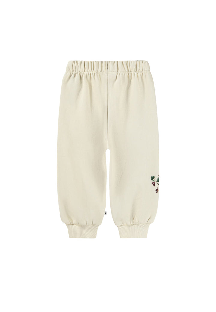 Back of Cream-colored jogger pants with an elastic waistband and cuffed ankles, featuring a small embroidered floral detail on the lower left leg.