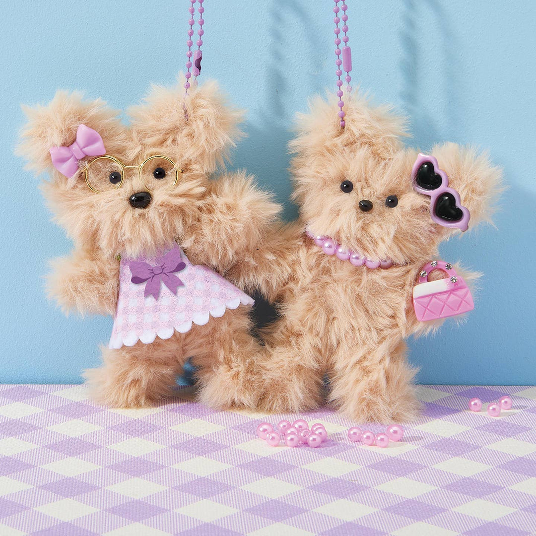 Two teddy bears dressed in pink outfits with accessories on a checkered tablecloth against a blue background.