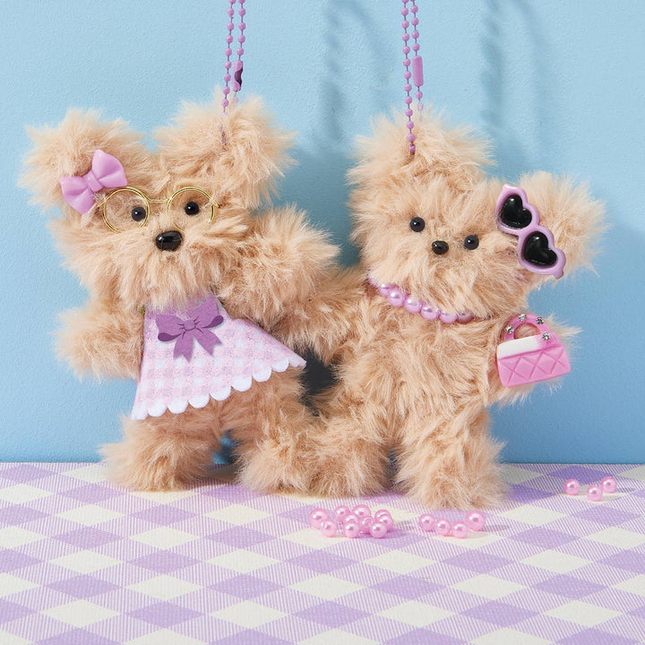 Two teddy bears dressed in pink outfits with accessories on a checkered tablecloth against a blue background.
