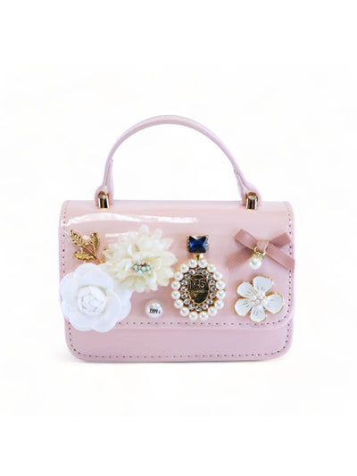 handbag in a light pink patent leather color with handle at the top. flower charms and pearl charms attached to the front flap. 