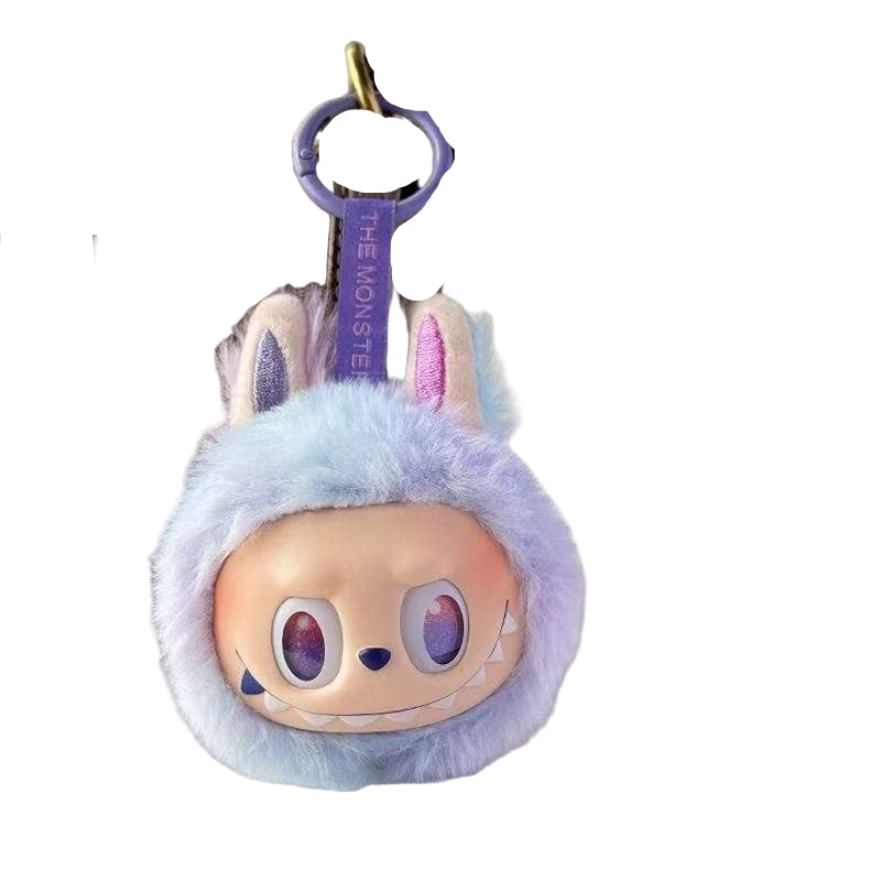 Plush keychain with cartoon face and bunny ears on a surface with a handbag and cup in the background.