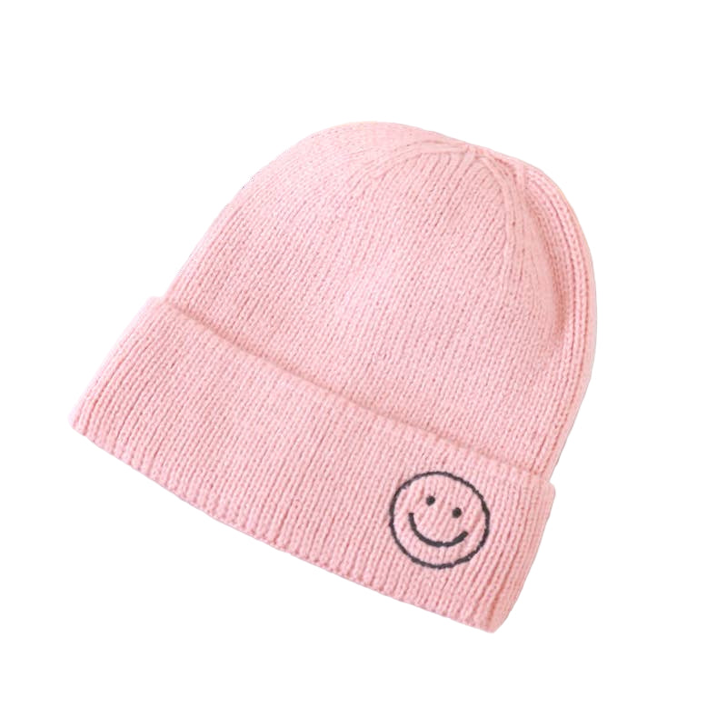 Pink knit beanie with a smiley face design on a light gray surface.