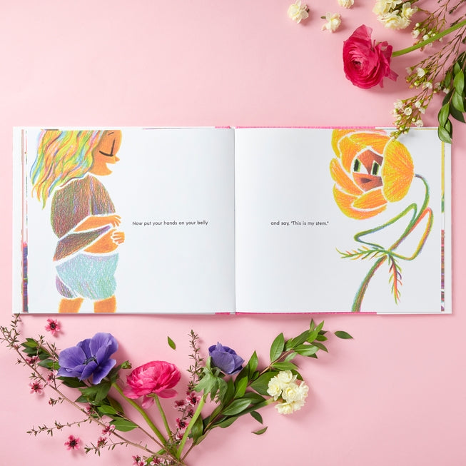 Open book with colorful illustrations of a woman and a flower on a pink background with flowers around.
