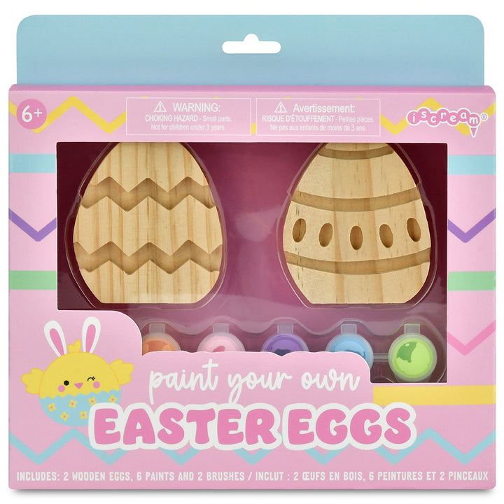 Packaged 'Paint Your Own Easter Eggs' craft set with wooden eggs, paints, and brushes on a pink background.