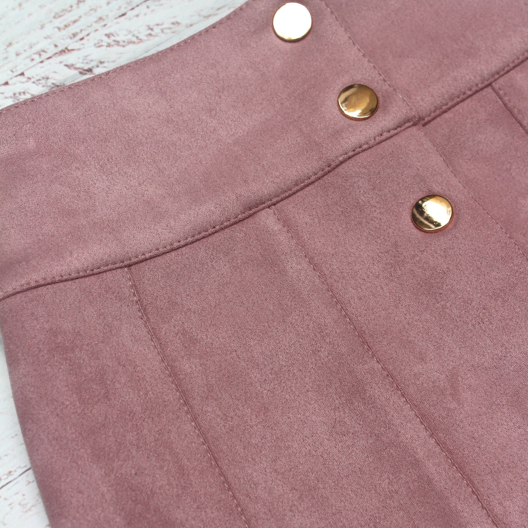 Close-up of a pink suede skirt with gold buttons on a light wooden surface