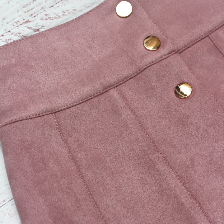 Close-up of a pink suede skirt with gold buttons on a light wooden surface