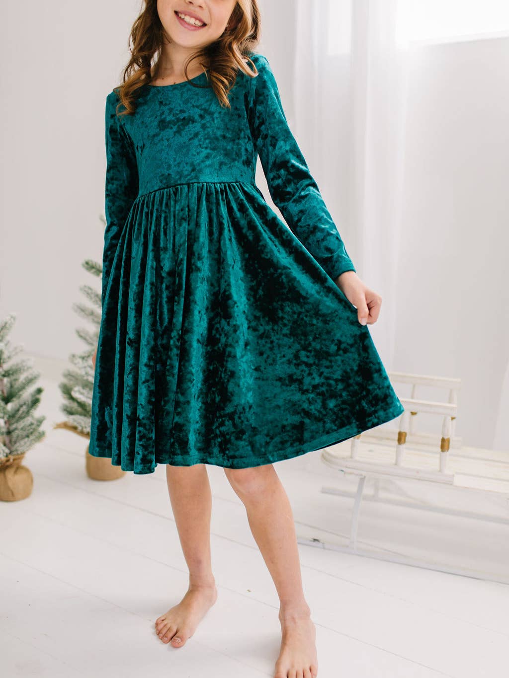 Young girl wearing a deep green velvet dress in a minimalistic room.