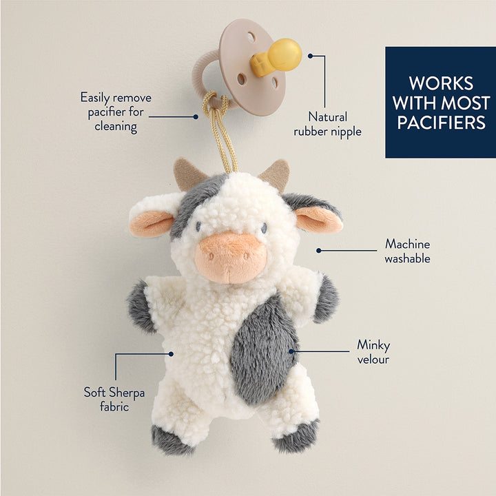 Plush cow pacifier holder with features highlighted on a light gray background