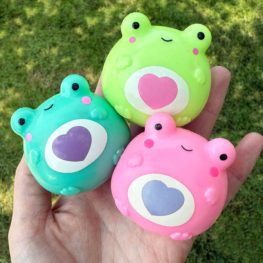 Three colorful frog-shaped objects with heart designs held in a hand against a grass background.