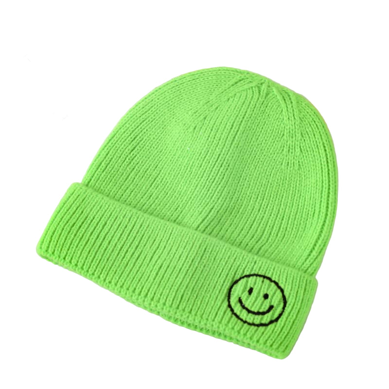 Green beanie with a smiley face design on a light gray surface.