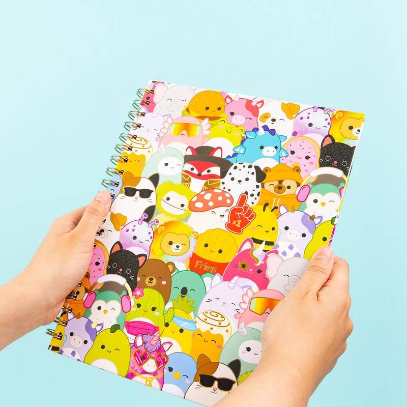 Notebook with colorful squishmallow animal pattern held by hands against a light blue background