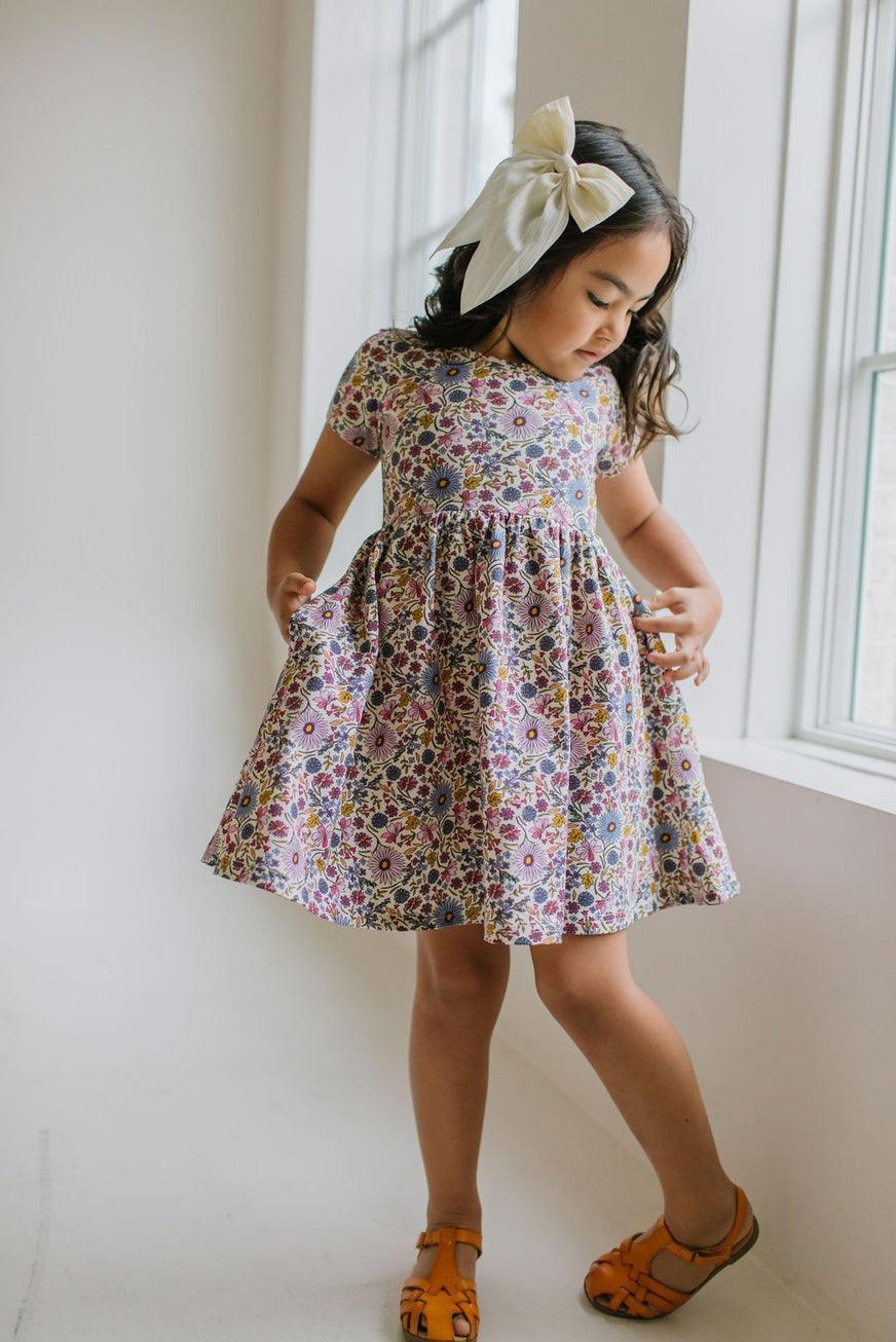 little girl wearing the floral dress with lavenders, purples, gold and pops of pink. 