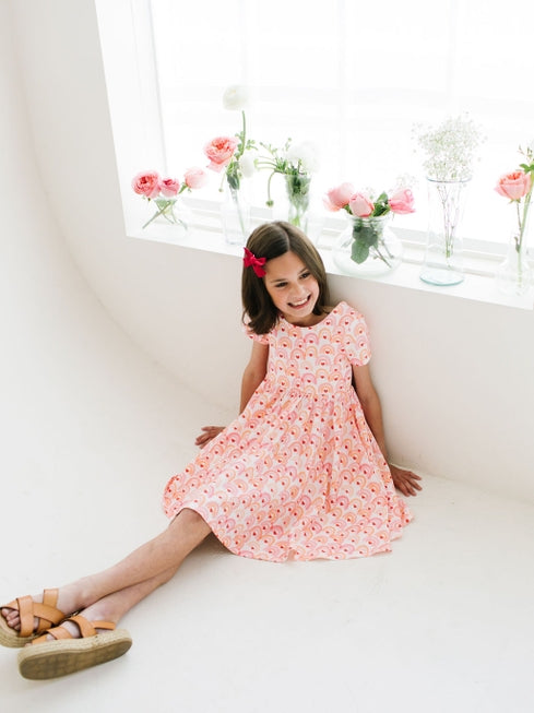 little girl modeling a scoop back dress with short sleeves, rainbows and hearts as an all over print 