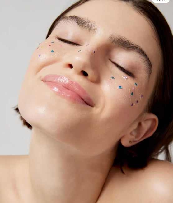 Close-up of a person with decorative glitter on her face on a plain background