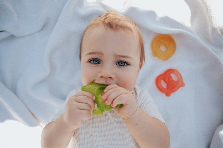 Baby chewing on a green teether with colorful letters in the background