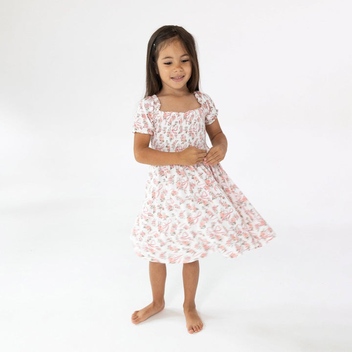 little girl twirling around in the dress with pink ribbons and pink rose bouquets all over the dress. 