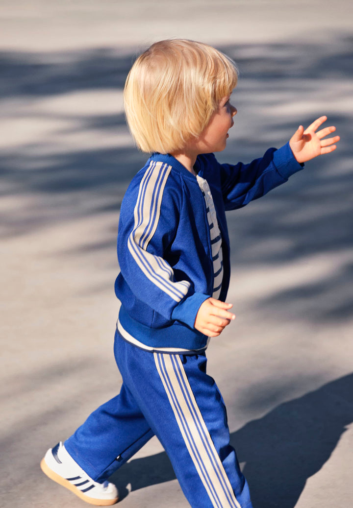 Child wearing a blue tracksuit with white stripes outdoors on a sunny day