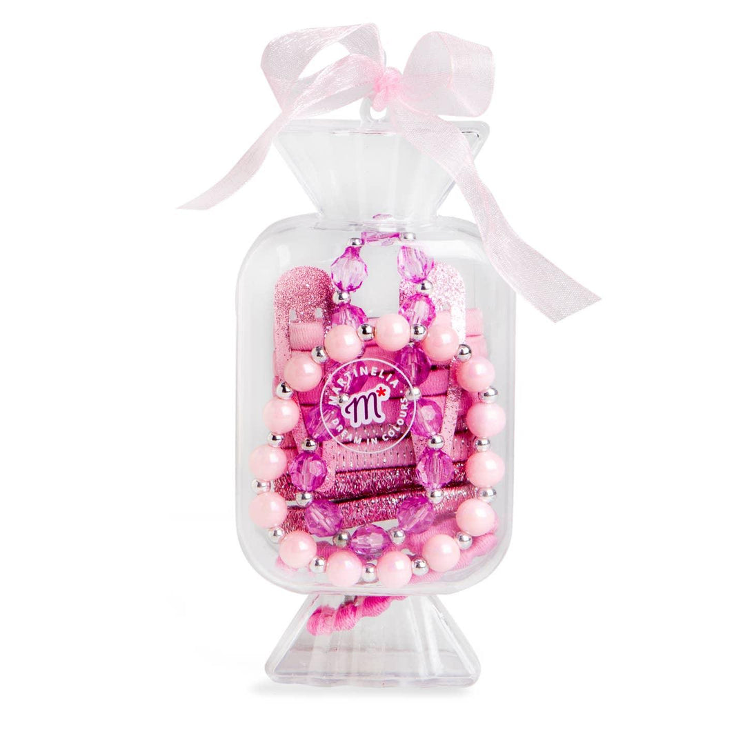 clear container shaped like a candy and topped with a pink ribbon. hair ties, bracelets and necklaces inside the clear candy container. 