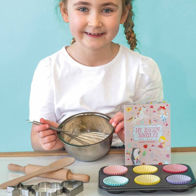 young girl sitting in front of the cooking set with wooden spoon, rolling pin and muffin tin and liners. 