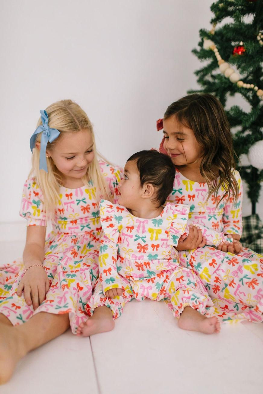 Three children in matching  with a colorful dresses with colroful bows on them Christmas tree in the background