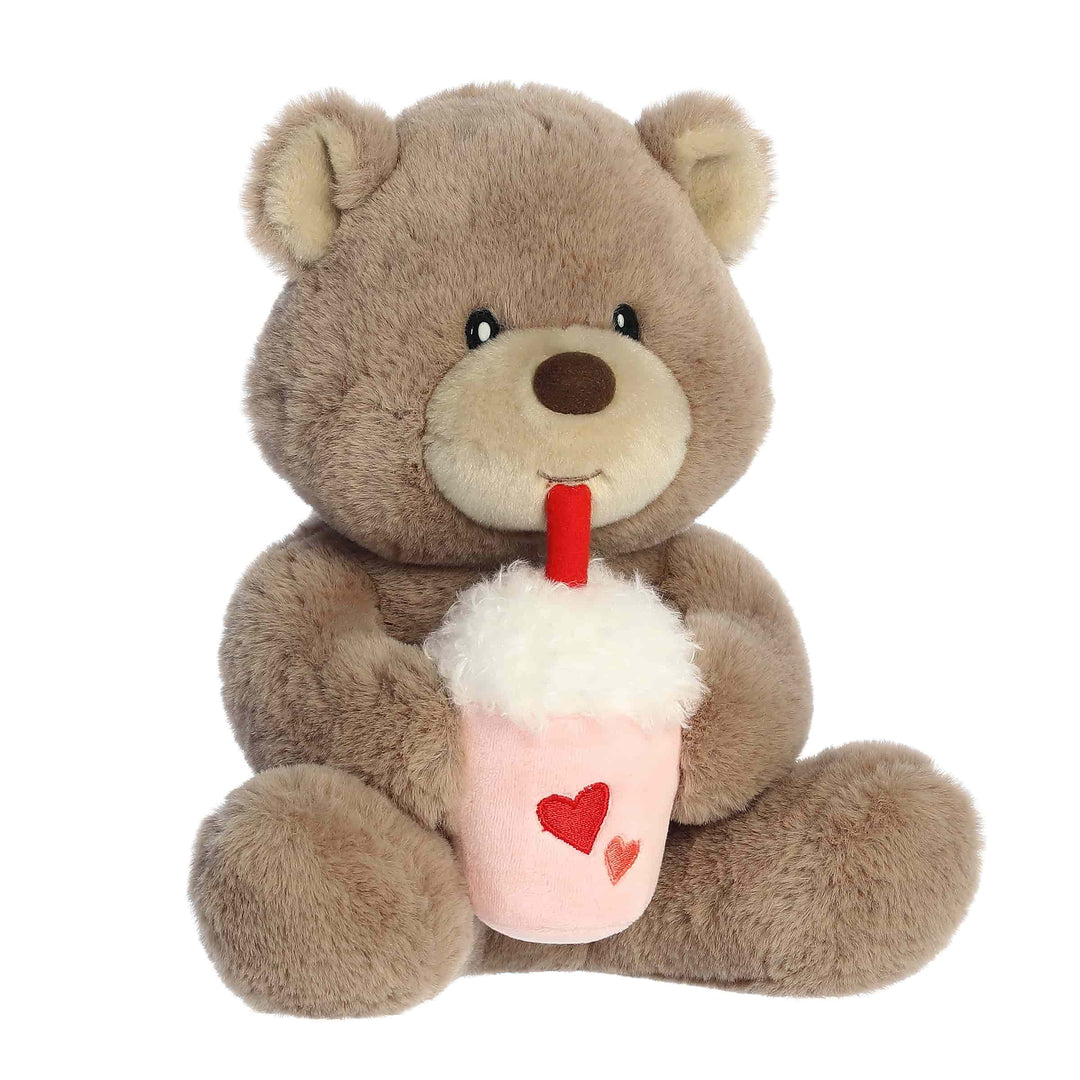 Plush teddy bear holding a pink cup with a red straw on a white background