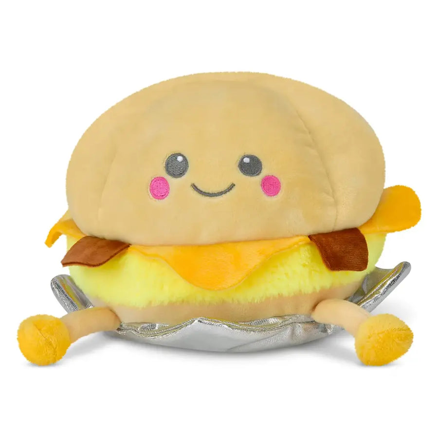 Plush toy resembling a bacon, egg and cheese sandwich with a smiling face on a white background