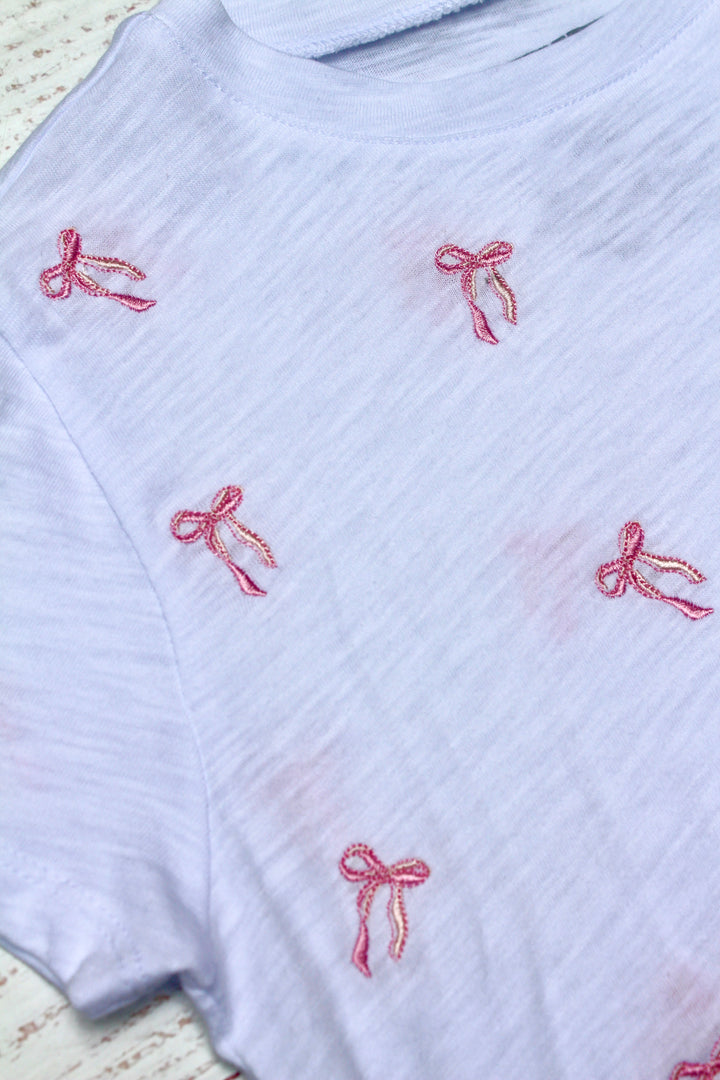 White ribbed sweater with red embroidered bows on a textured background
