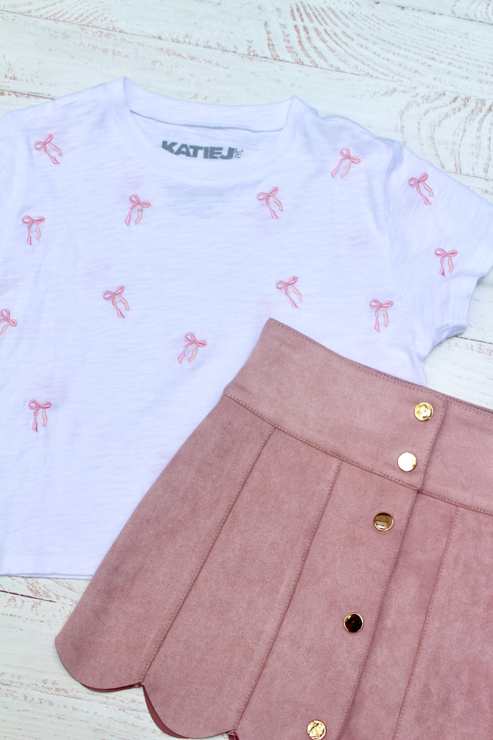 White shirt with pink bow pattern and pink skirt on a light wooden surface