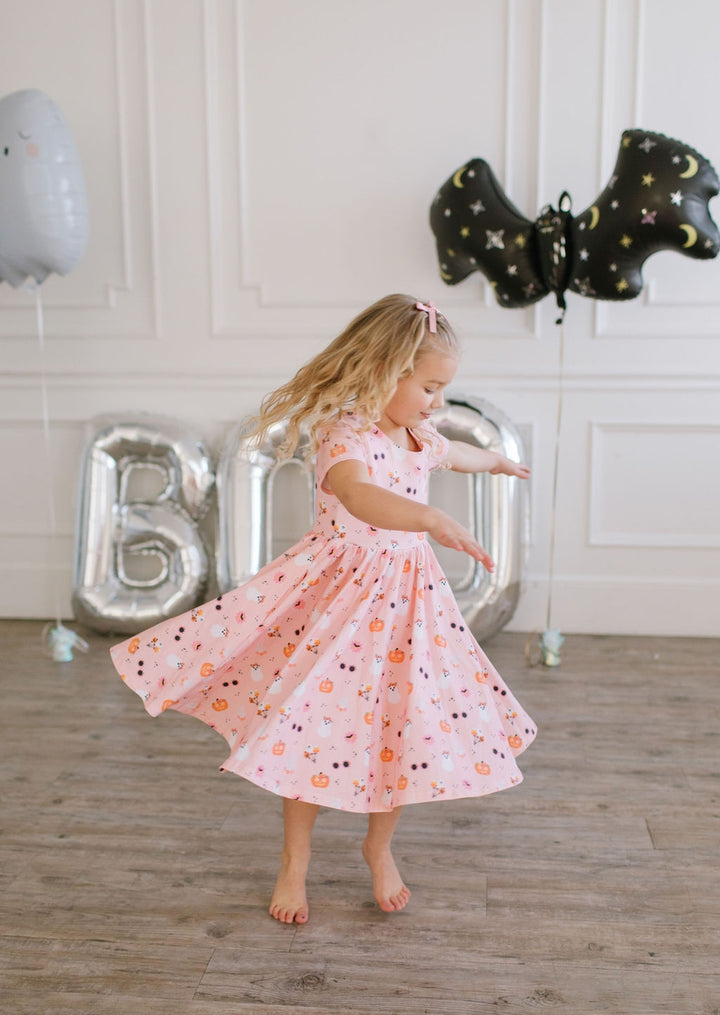 Young girl in a floral dress standing in front of balloons spelling 'BOo' in a room.