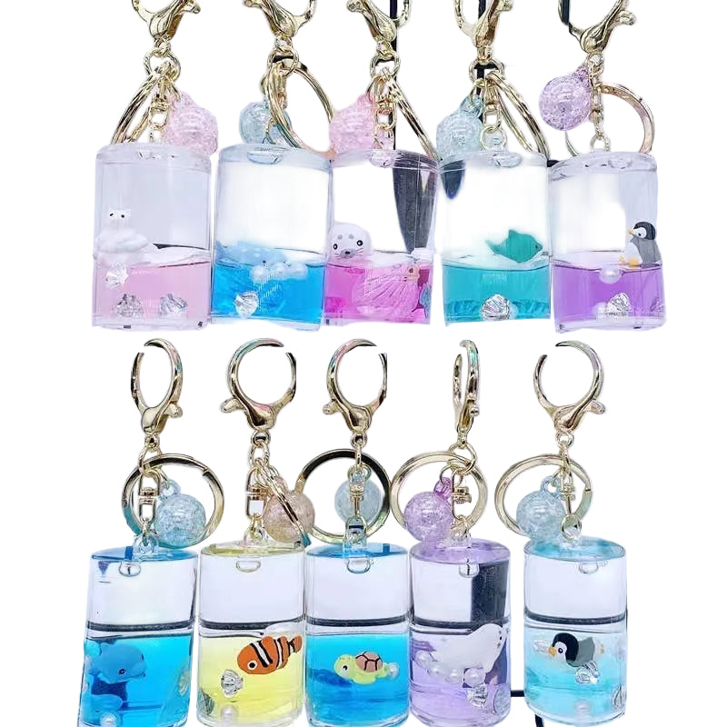Keychains with small aquarium-style compartments containing various sea-themed figurines on a grid background.