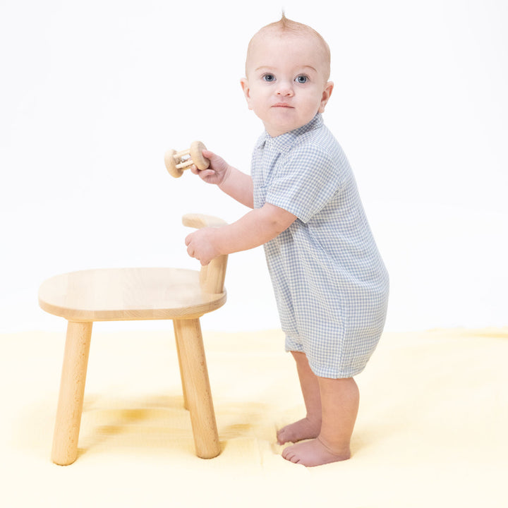 Baby standing next to a small wooden stool on a white background