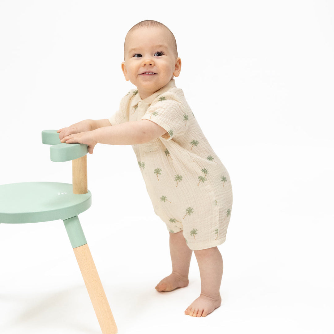 Baby standing next to a green and wooden stool on a white background