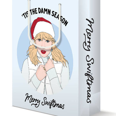 white gift bag with a drawing of Taylor Swift on it that says 'Tis the Damn Season' 'Merry Swiftmas' 