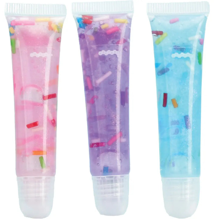 Three colorful lip balms with sprinkles in pink, purple, and blue on a white background.