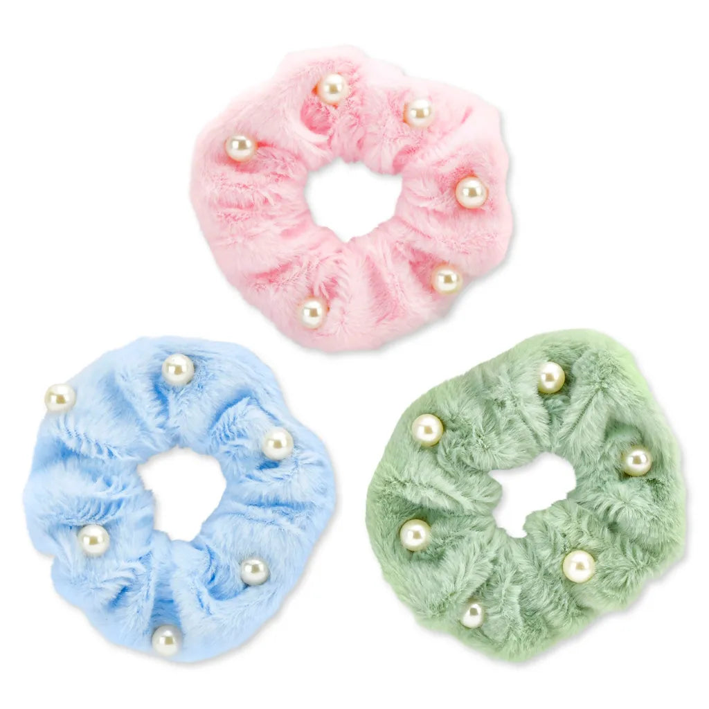 Three fuzzy faux-fur hair scrunchies in pastel pink, light blue, and mint green, each decorated with small white faux pearls, arranged on a plain white background.