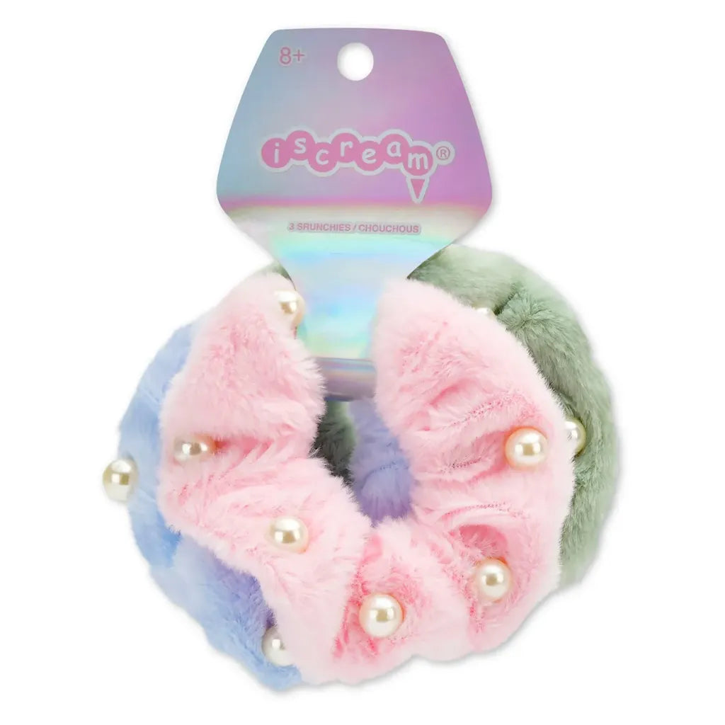A set of three pastel-colored fuzzy hair scrunchies with pearl embellishments, attached to a holographic 'iscream' brand card. The scrunchies are pink, light blue, and sage green.