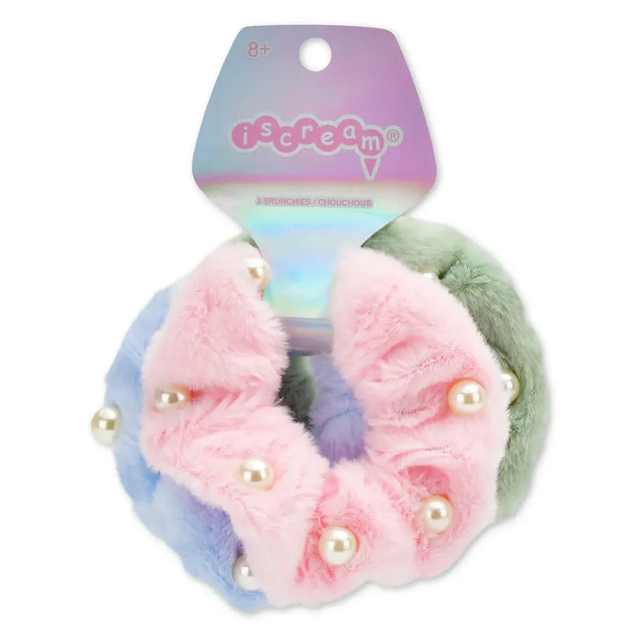 A set of three pastel-colored fuzzy hair scrunchies with pearl embellishments, attached to a holographic 'iscream' brand card. The scrunchies are pink, light blue, and sage green.