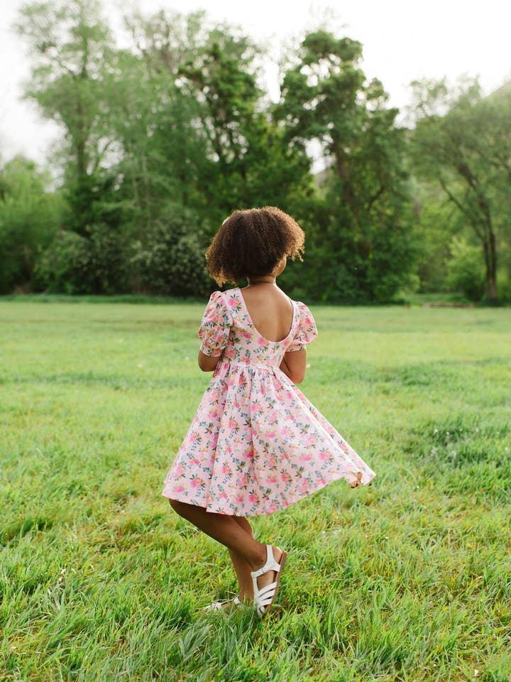 this picture shows a little girl modeling the peach floral dress with puff sleeves and pretty cabbage floral print. the back has a scoop back