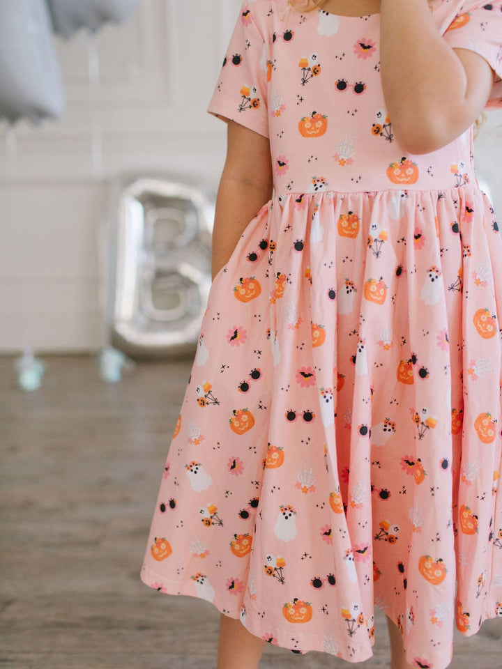 Person wearing a pink dress with Halloween-themed patterns in a blurred indoor setting