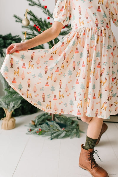 girl extending the skirt of her dress showing the print of the dress as Nutcracker with green and pink trees as well as reindeer and Nutcracker 